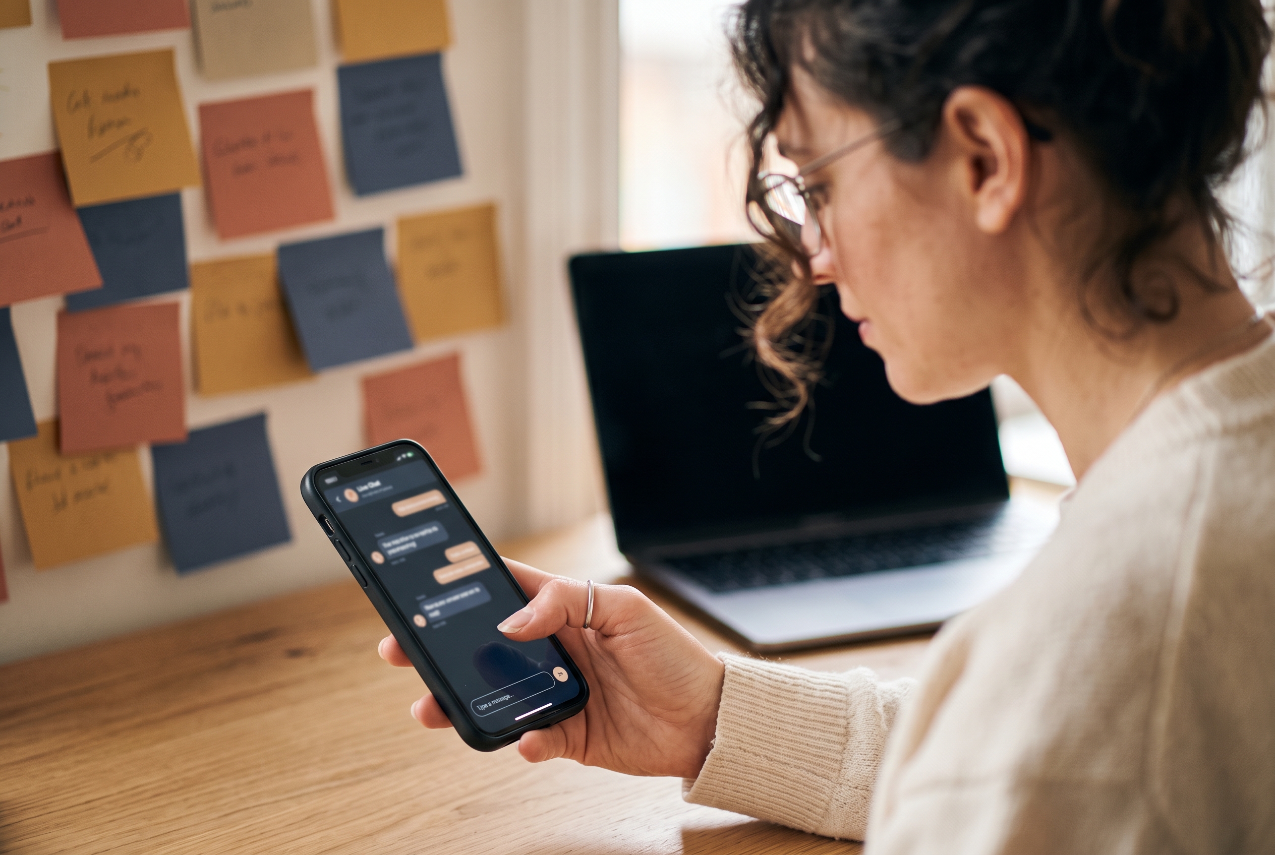 Ecommerce manager testing a live chat widget on a phone while sitting at a desk with sticky notes on the wall