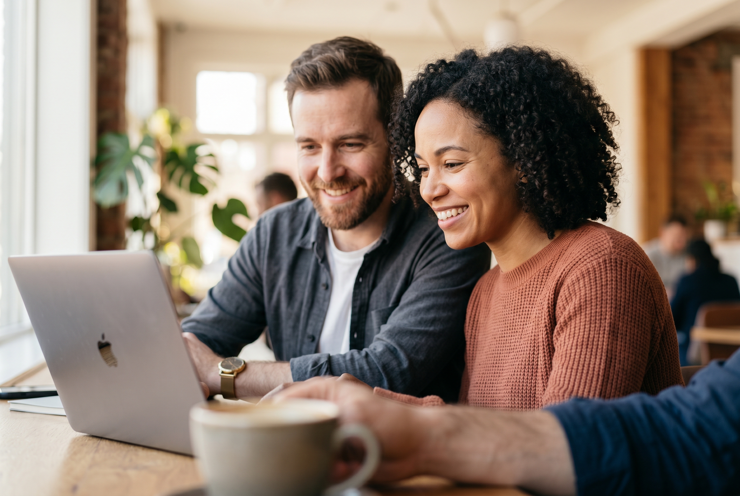 Two co-founders smiling at a shared laptop screen reviewing their new online store in a bright coworking space