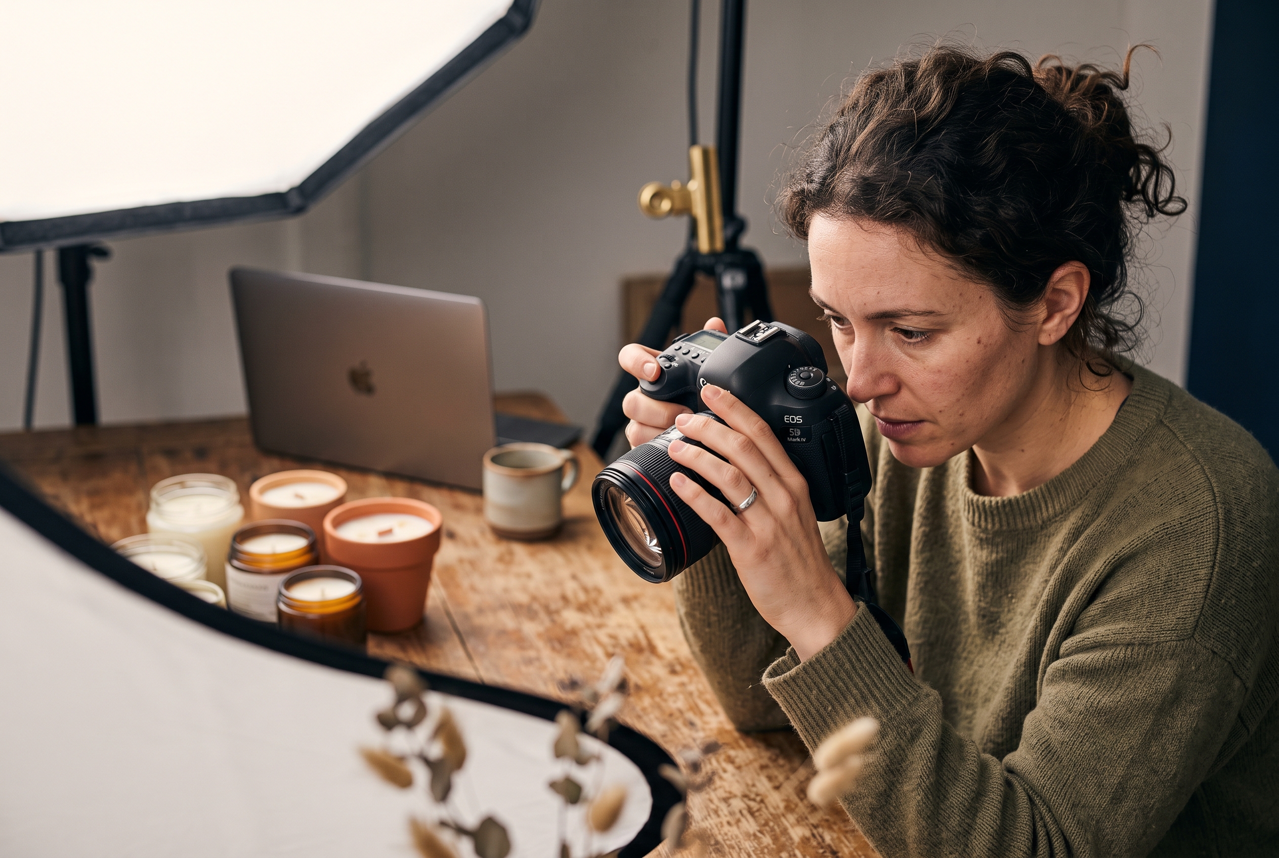 Woman photographing handmade candles on a wooden table with a softbox light in a home studio