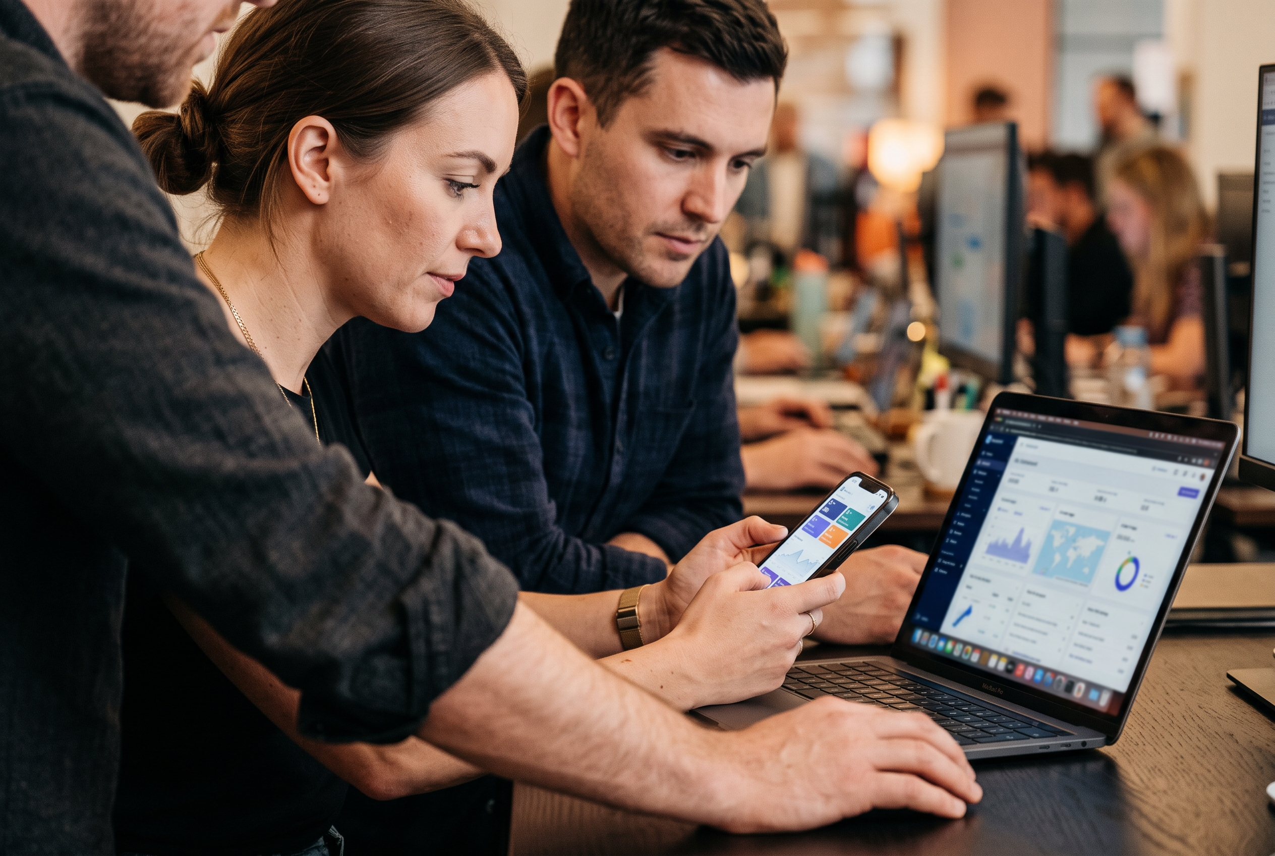 Two colleagues at a standing desk checking a live store on phone and laptop during a launch cutover